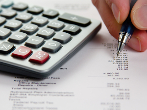 Hand holding a pen next to a calculator marking up tax documents